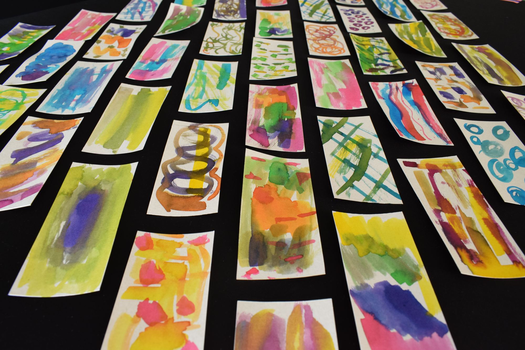 Decenas de tarjetas pintadas en acuarela por participantes, sobre una mesa negra
