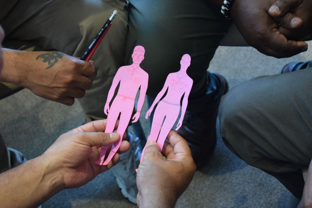 Dos participantes sostienen siluetas de papel rosado que dibujaron