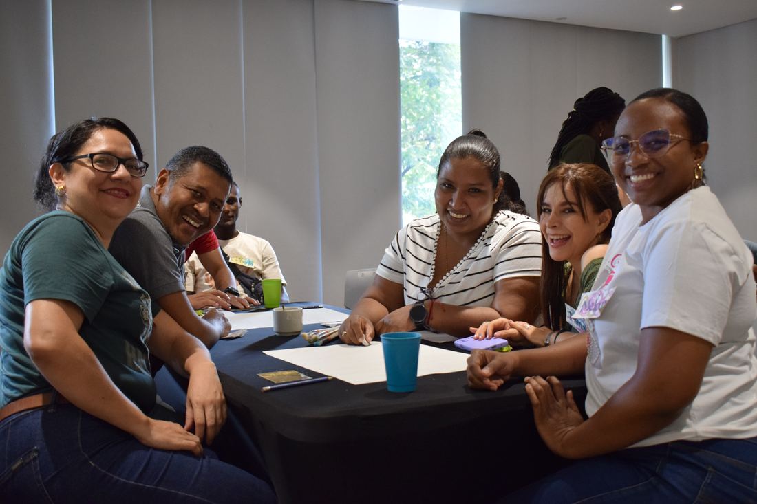 Participantes sonríen alrededor de una mesa de trabajo